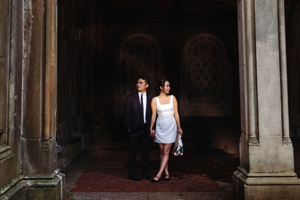 Elegantly dressed couple walks through grand archway of historic building.