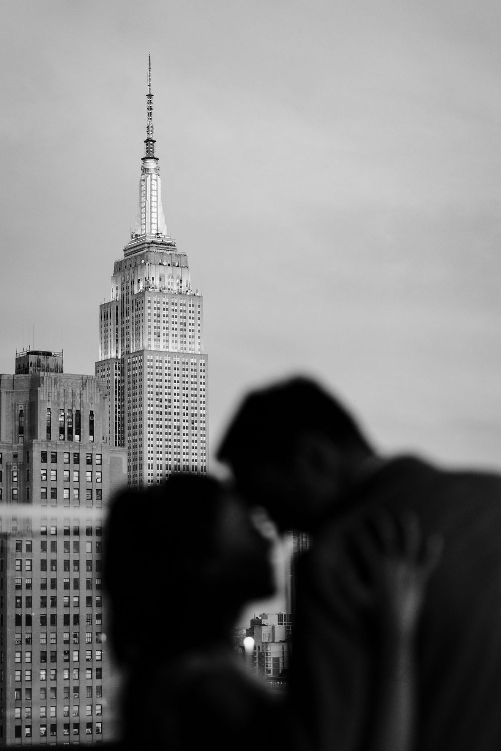 Black and white cityscape showing the Empire State Building and surrounding skyscrapers against a cloudy sky.