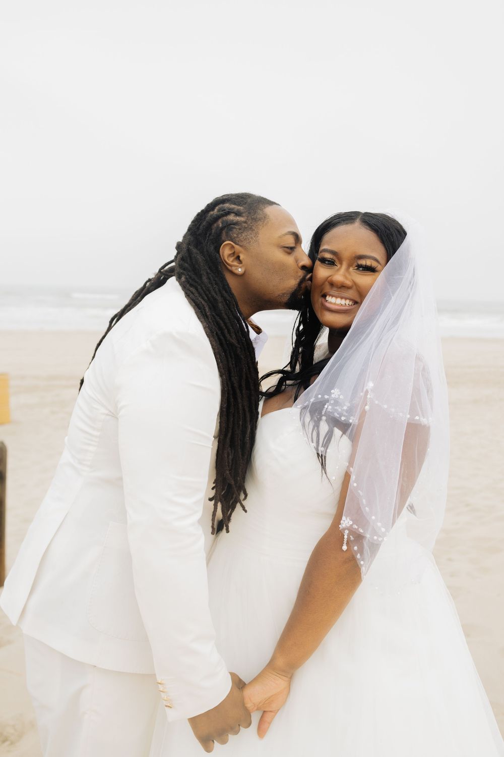 Happy couple in white wedding attire sharing joyful moment on beach.