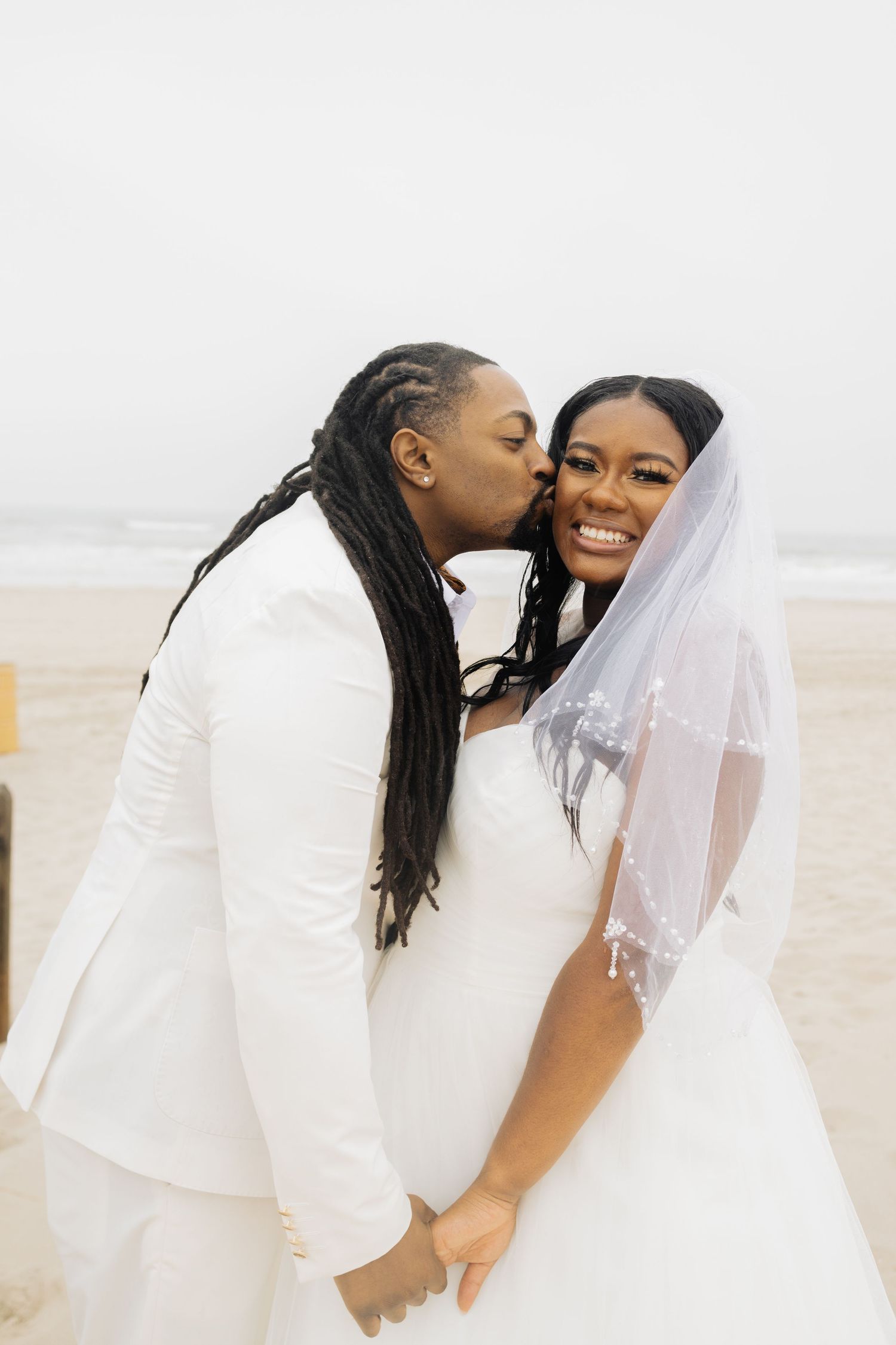 Happy couple in white wedding attire sharing joyful moment on beach.