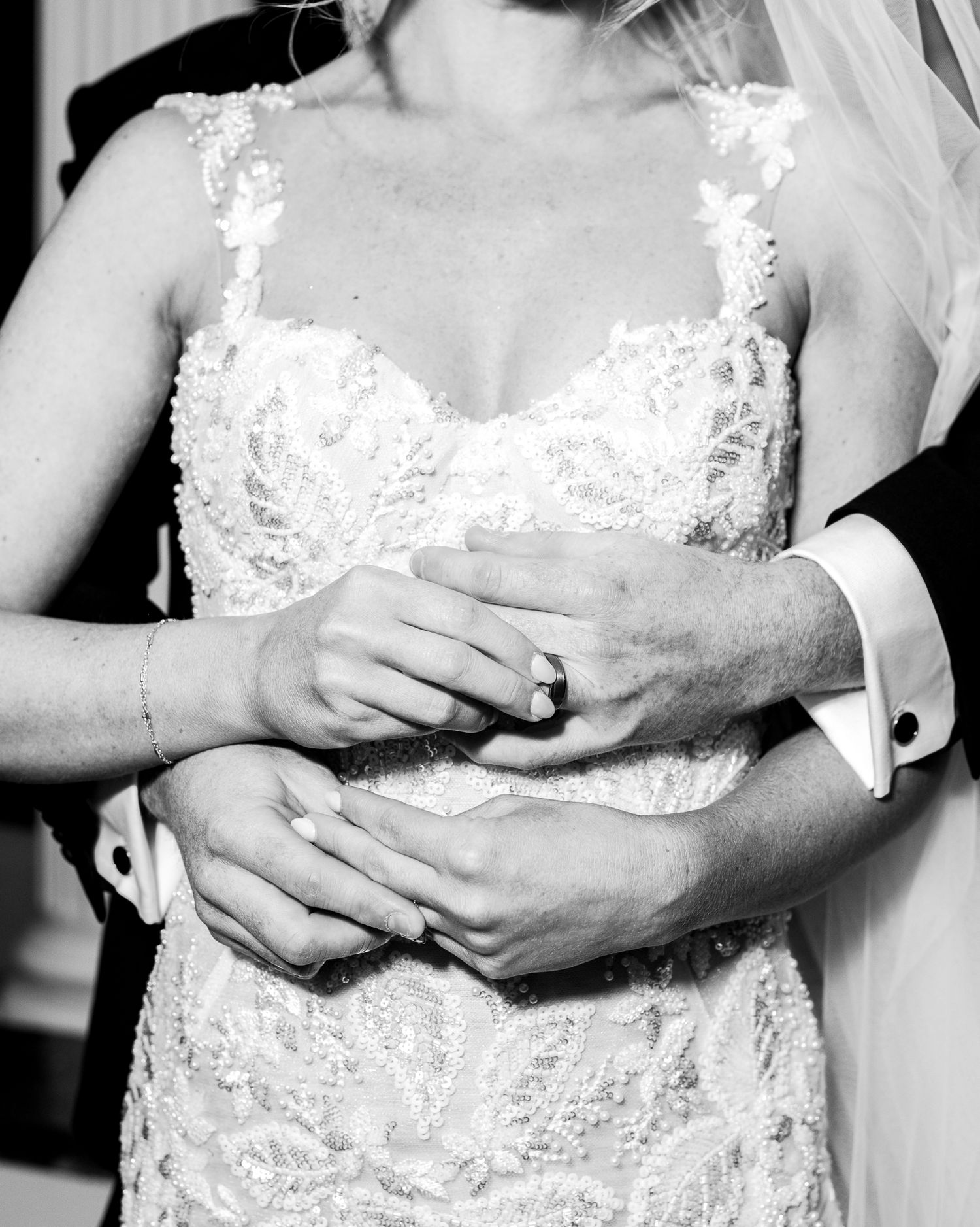 Close-up detail shot of a white lace wedding dress bodice showing delicate floral patterns and beading.
