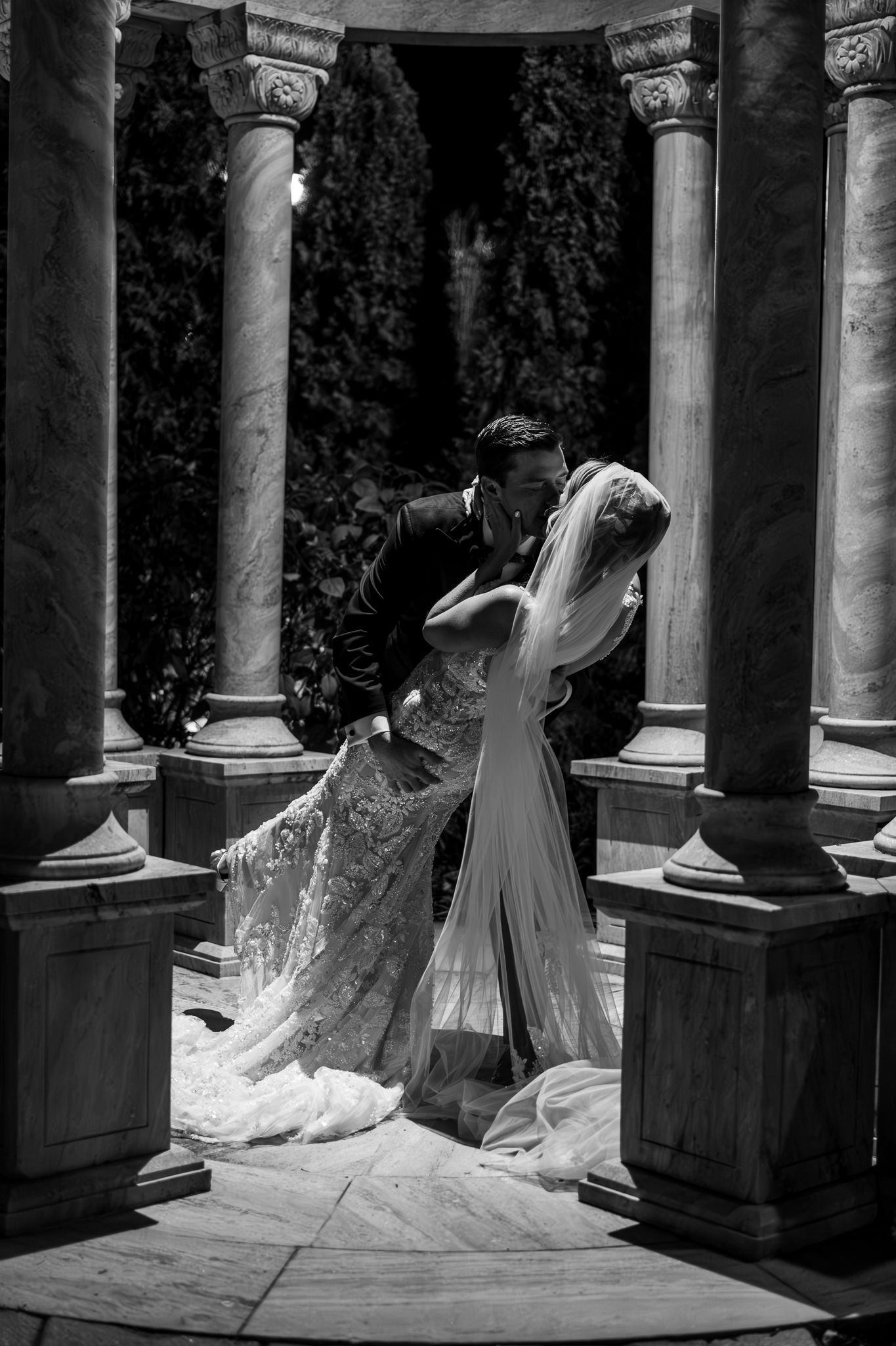 A black and white artistic sequence showing a flowing wedding dress moving gracefully between classical columns.