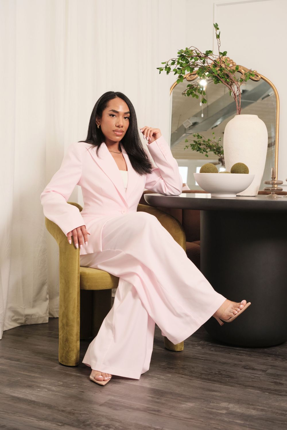 Model in flowing pink loungewear poses elegantly on hardwood floor with indoor plants.