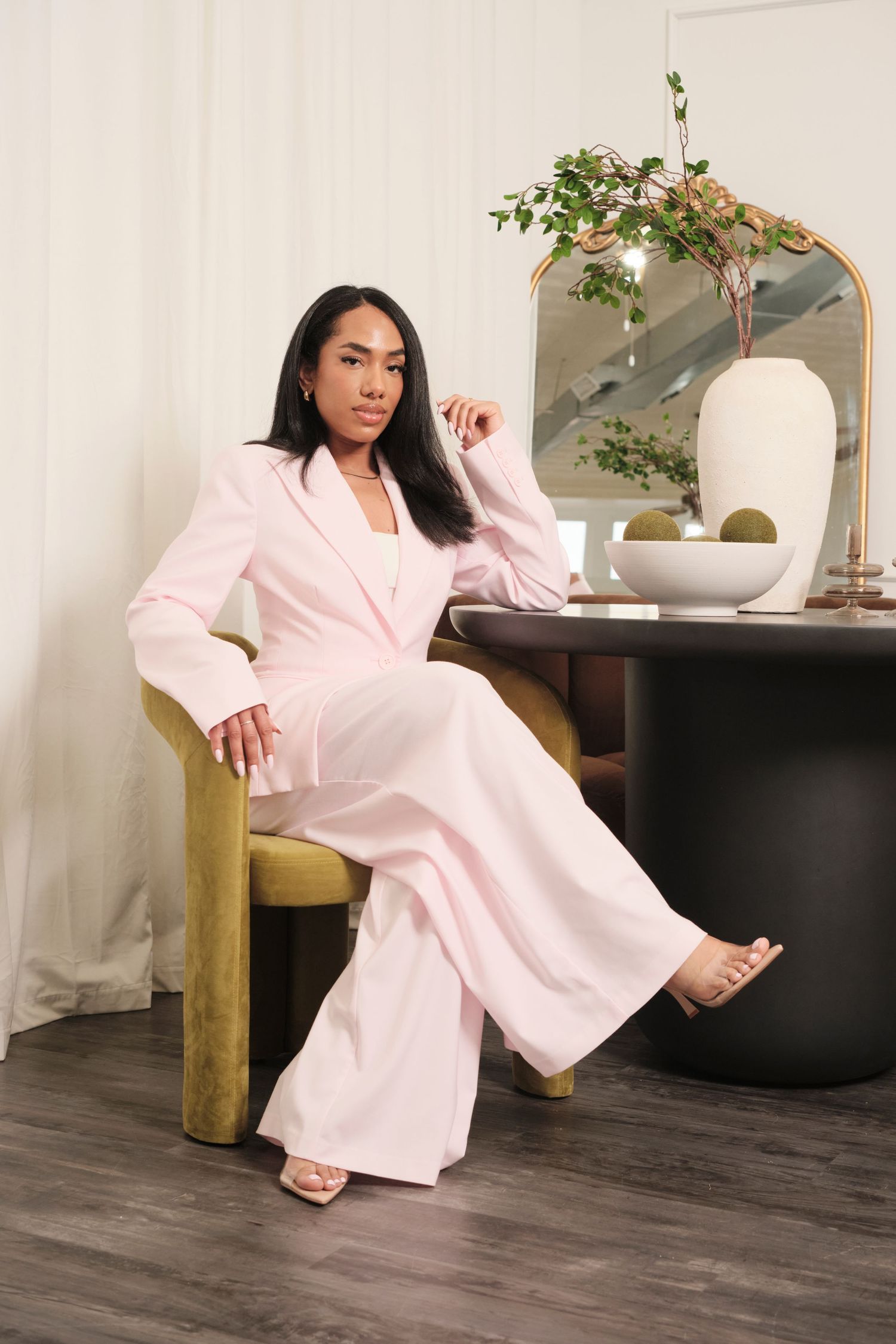 Model in flowing pink loungewear poses elegantly on hardwood floor with indoor plants.