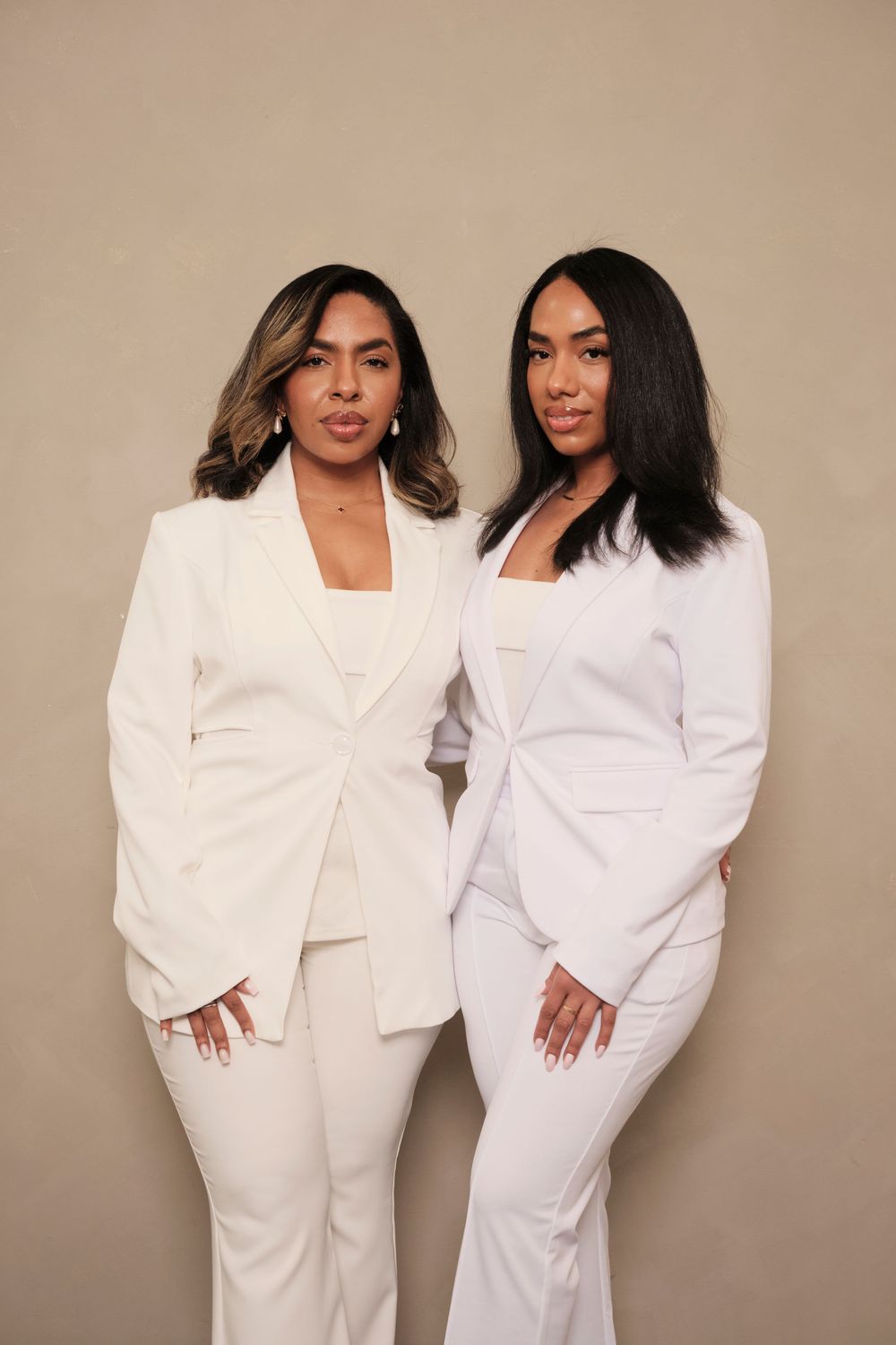 Two professionals in matching white business suits pose together against neutral background.