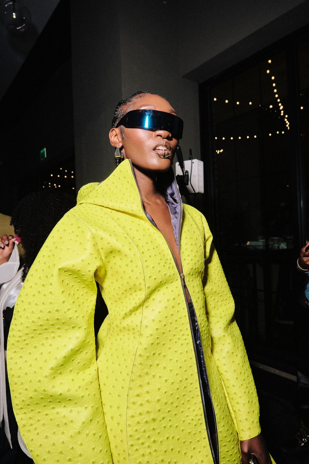 Stylish figure in bright neon yellow textured jacket poses at a nighttime event.