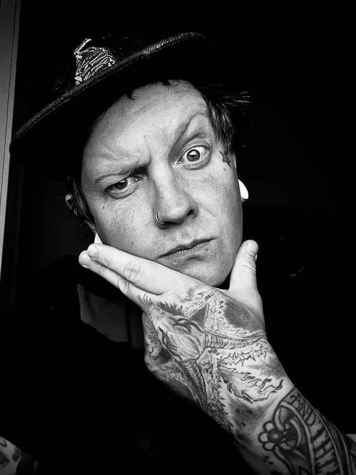 Dramatic black and white portrait showing tattooed hand gesture against dark background.