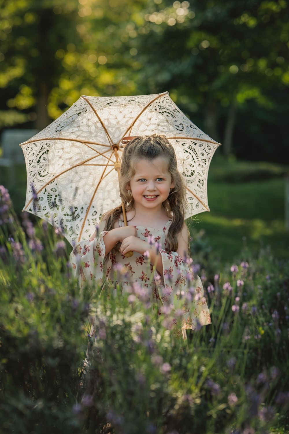 4 year old girl with brown curls and lace parasol smiling in row of lavender