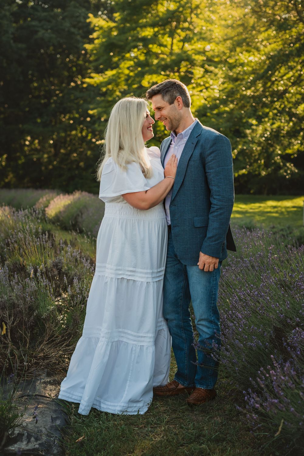 husband and wife stare lovingly at each other in a row of lavender bushes