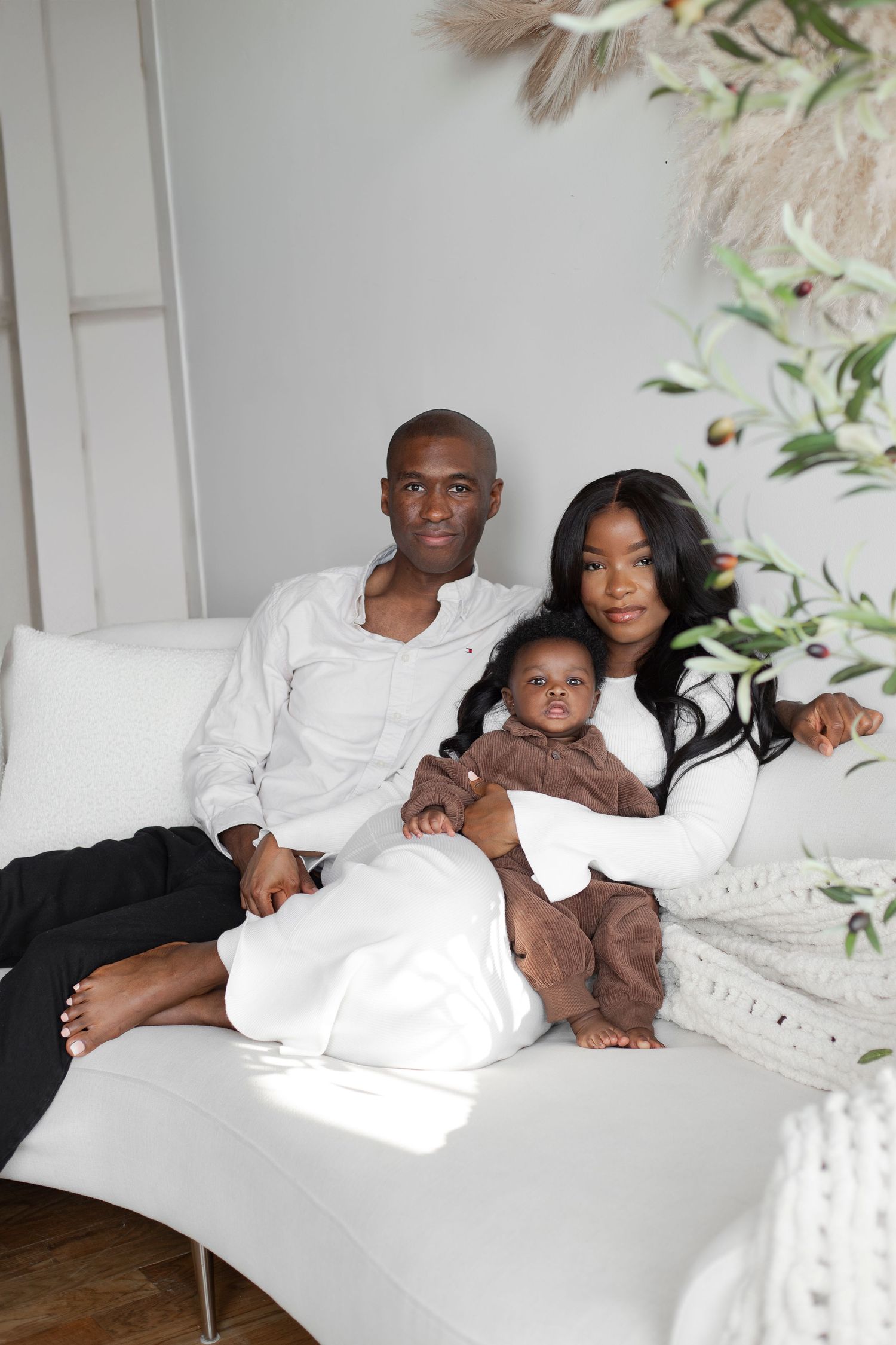 Beautiful family portrait lounging together on a white couch with delicate foliage decor in the background.