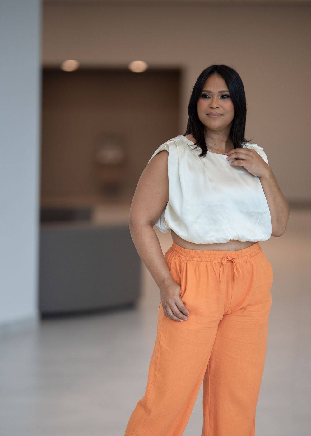 Professional wearing white top and orange pants in modern office setting.