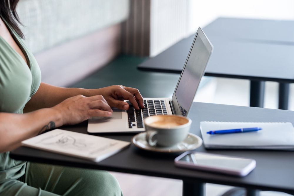 Close up of hands typing on laptop with coffee cup on desk.