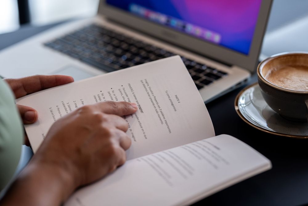 Person reviewing documents with laptop and coffee cup on desk.