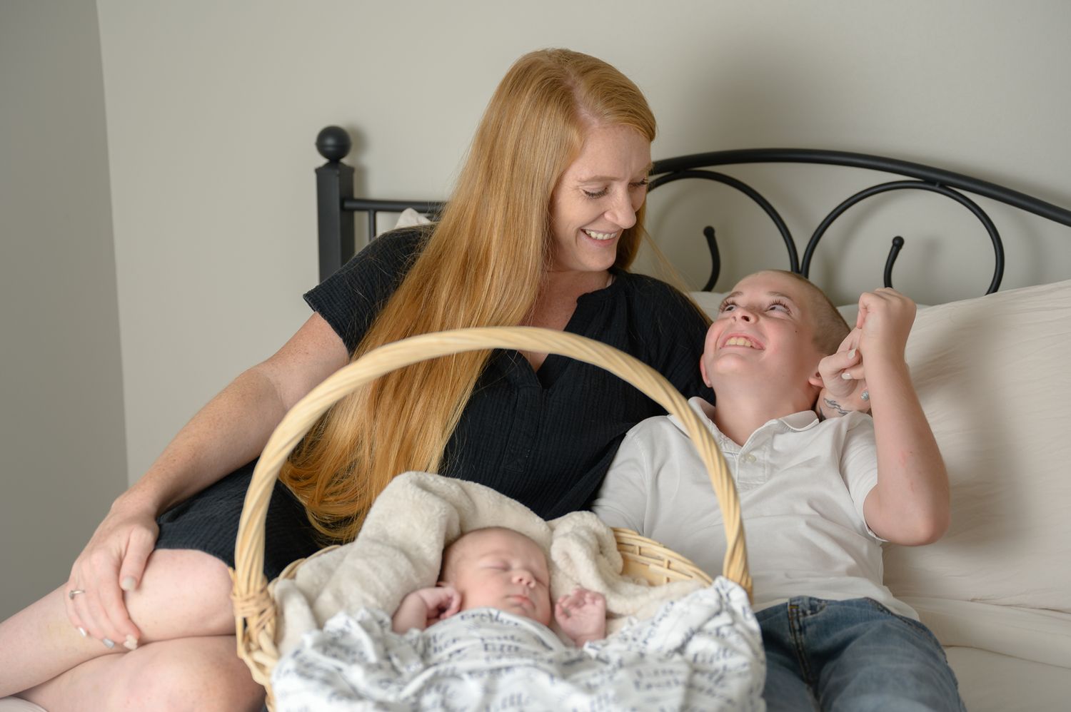 Family members relaxing on bed with wicker basket containing sleeping infant.