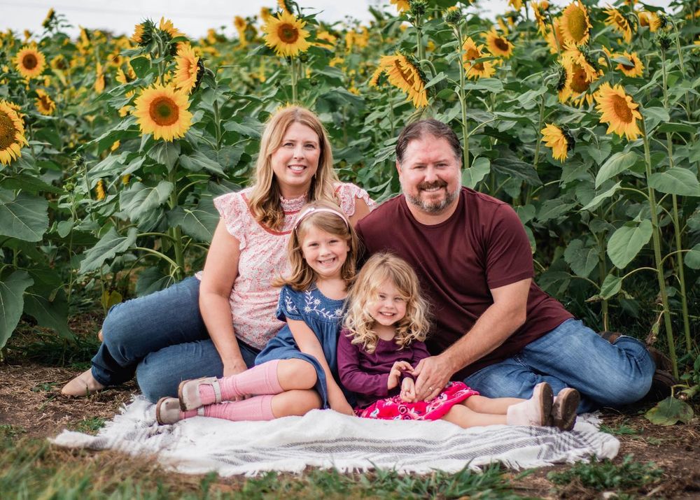 A loving family portrait taken in front of towering sunflowers on a sunny day.