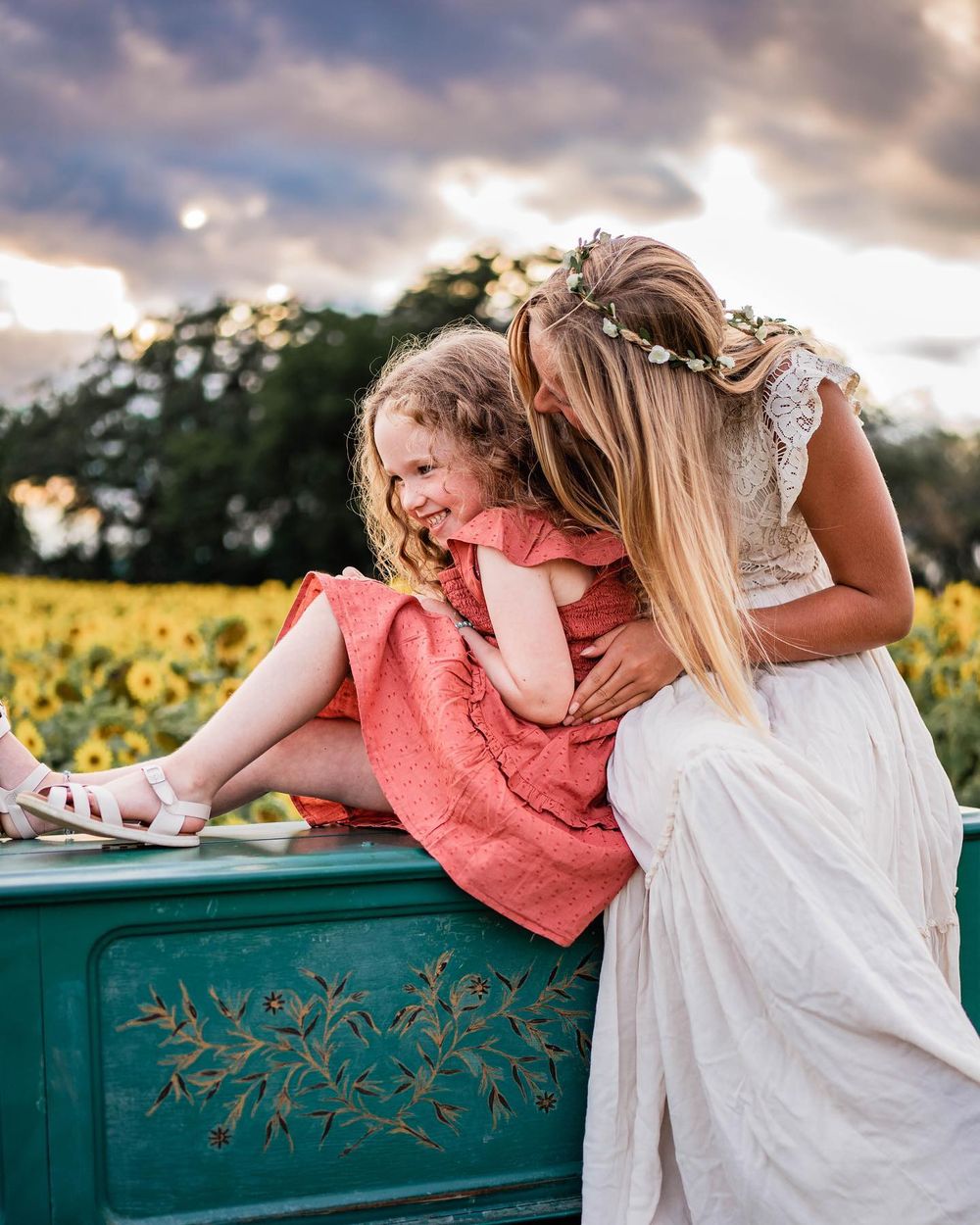 Sweet moment between two people sitting on vintage turquoise piano in sunflower field.