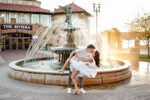 A romantic couple poses near a fountain during golden hour sunset creating an ethereal wedding photography moment.