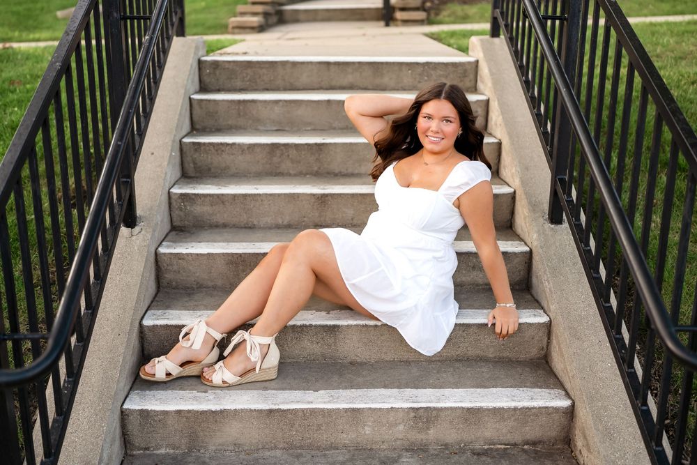 Person in a white dress seated on outdoor concrete stairs in a relaxed pose.