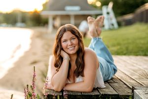 A person poses lying on a wooden deck during a sunny outdoor photo session at golden hour.