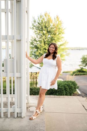 A person in a white dress poses playfully across three artistic architectural columns at an outdoor venue.
