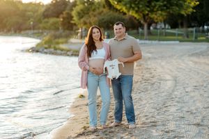A couple stands together on a sandy beach at sunset holding beverages while enjoying a warm evening.
