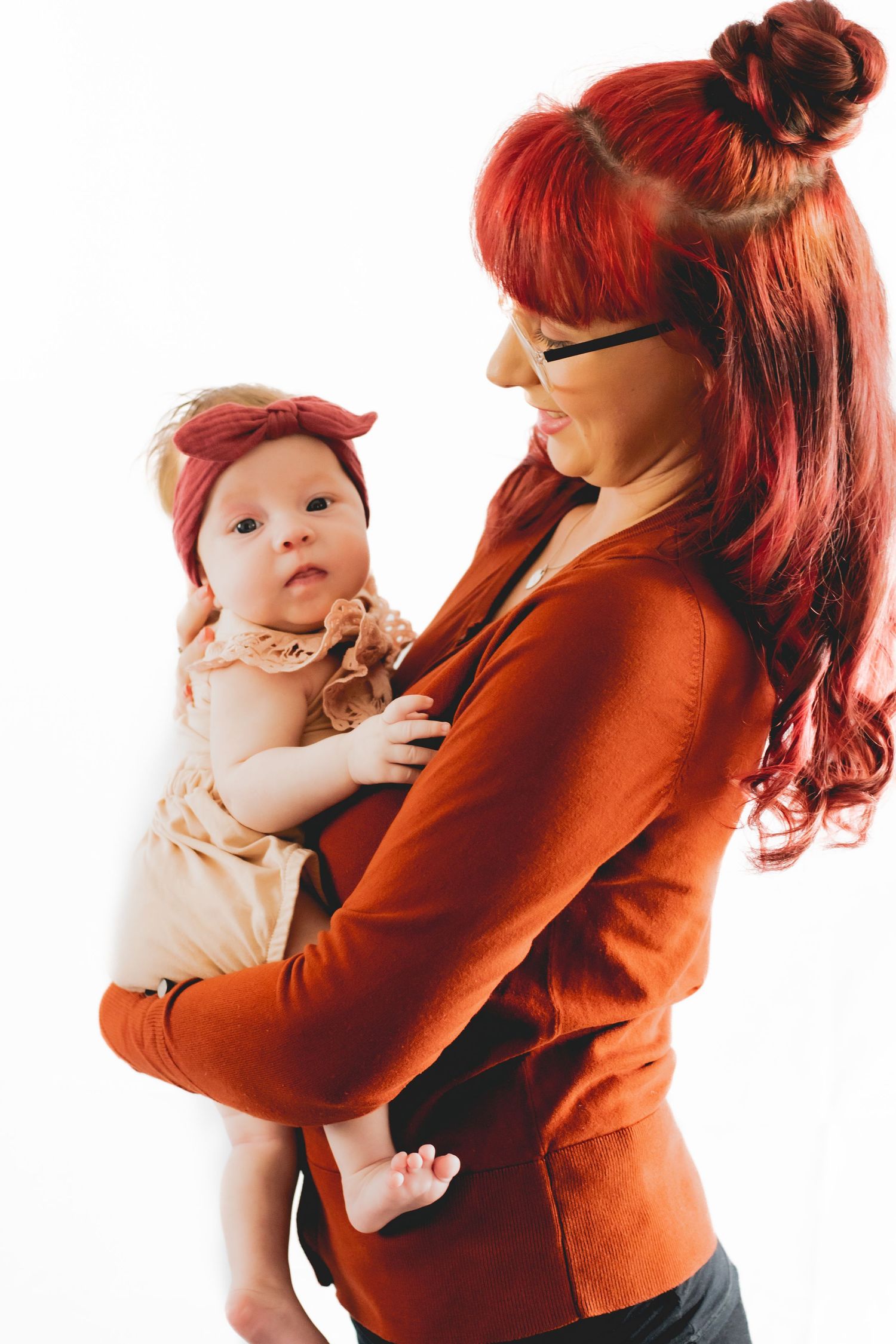 A woman in a red sweater holds a small baby wearing a peach-colored outfit.