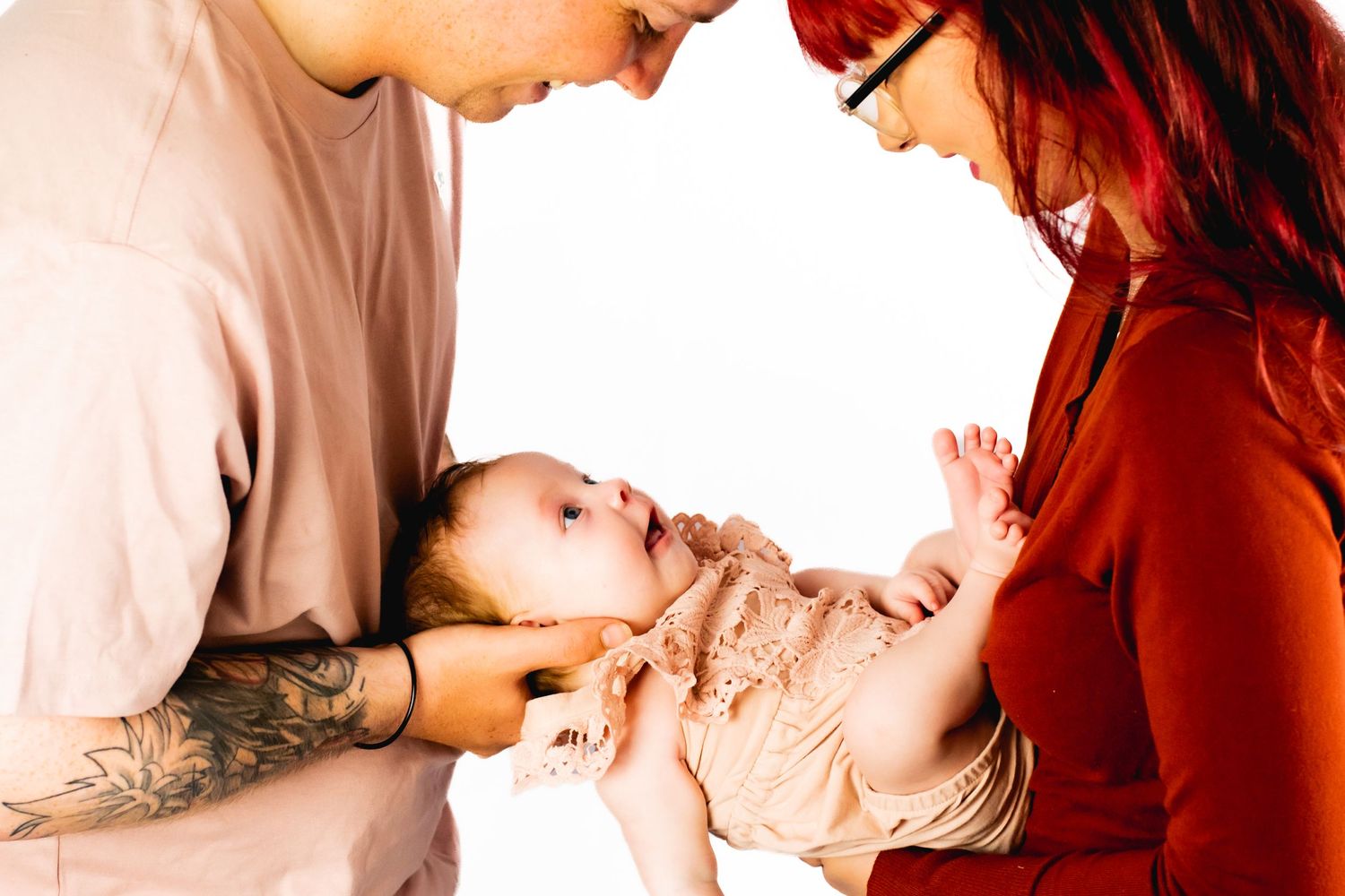 Parents in pink and rust colors gazing down at their smiling baby.