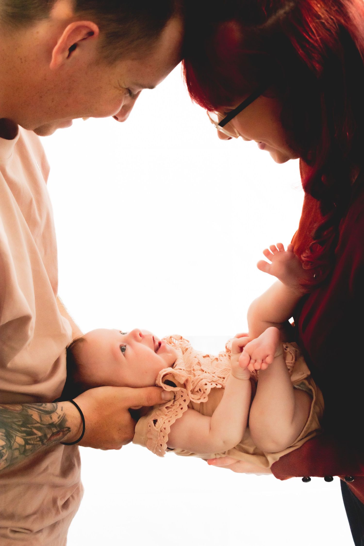 Parents in red and pink lean over their baby lying between them.