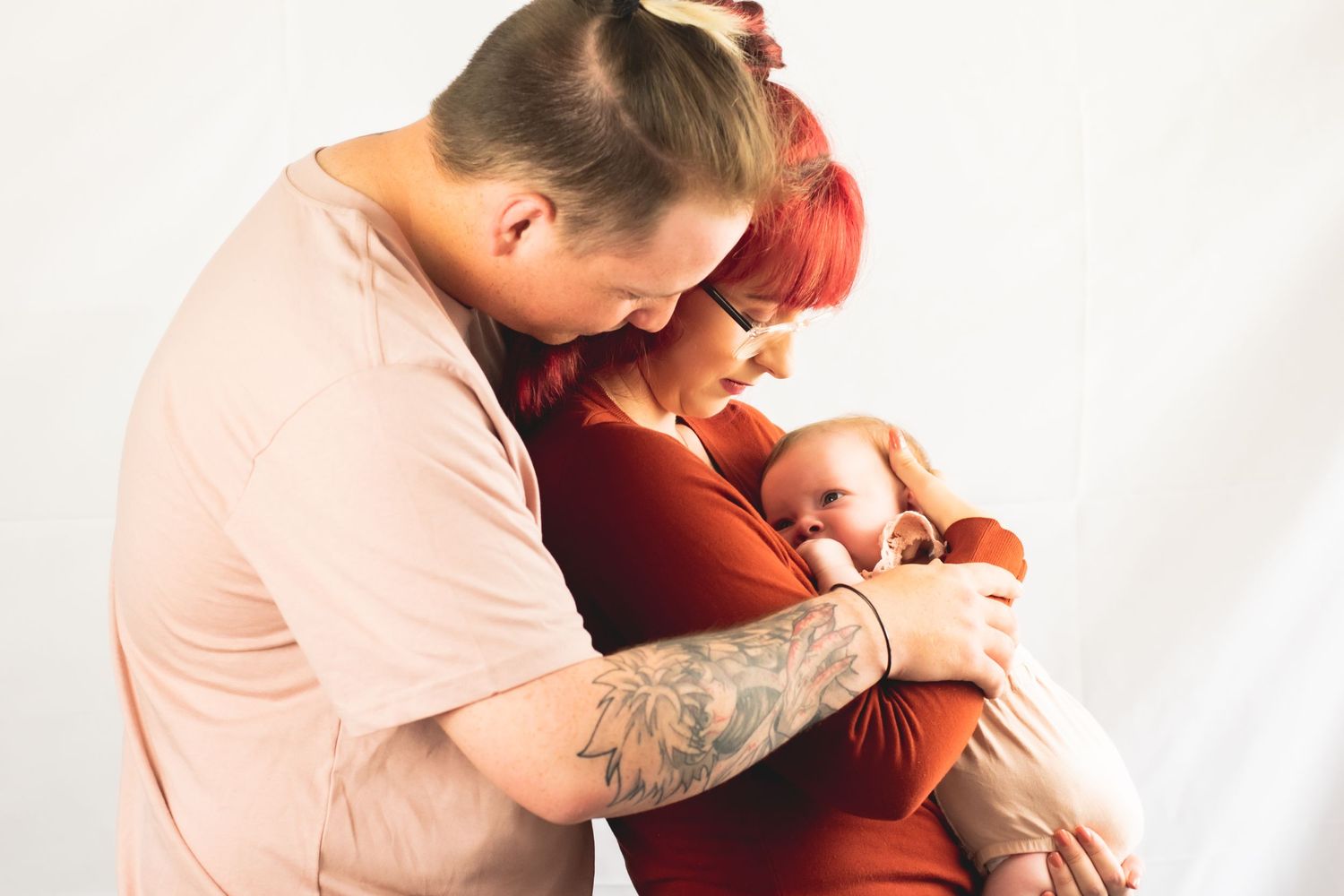 Parents in pink and rust colors share an intimate moment while holding their baby.