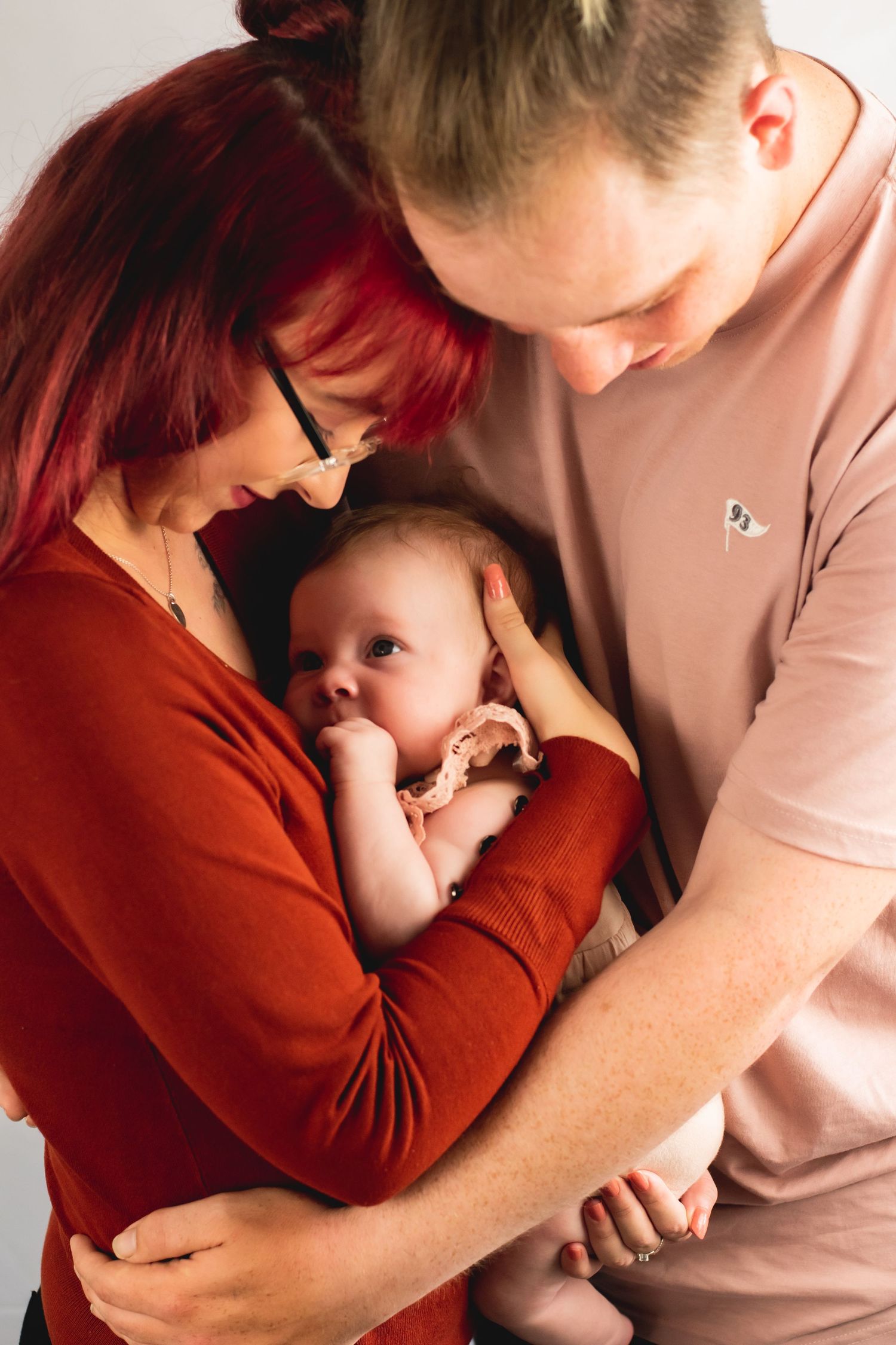 A couple in red and pink shirts lovingly hold their baby between them.