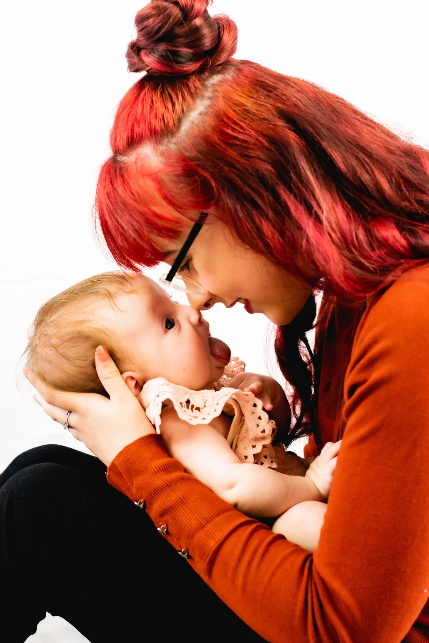 Close up of parent with vibrant red hair nuzzling baby in orange outfit.