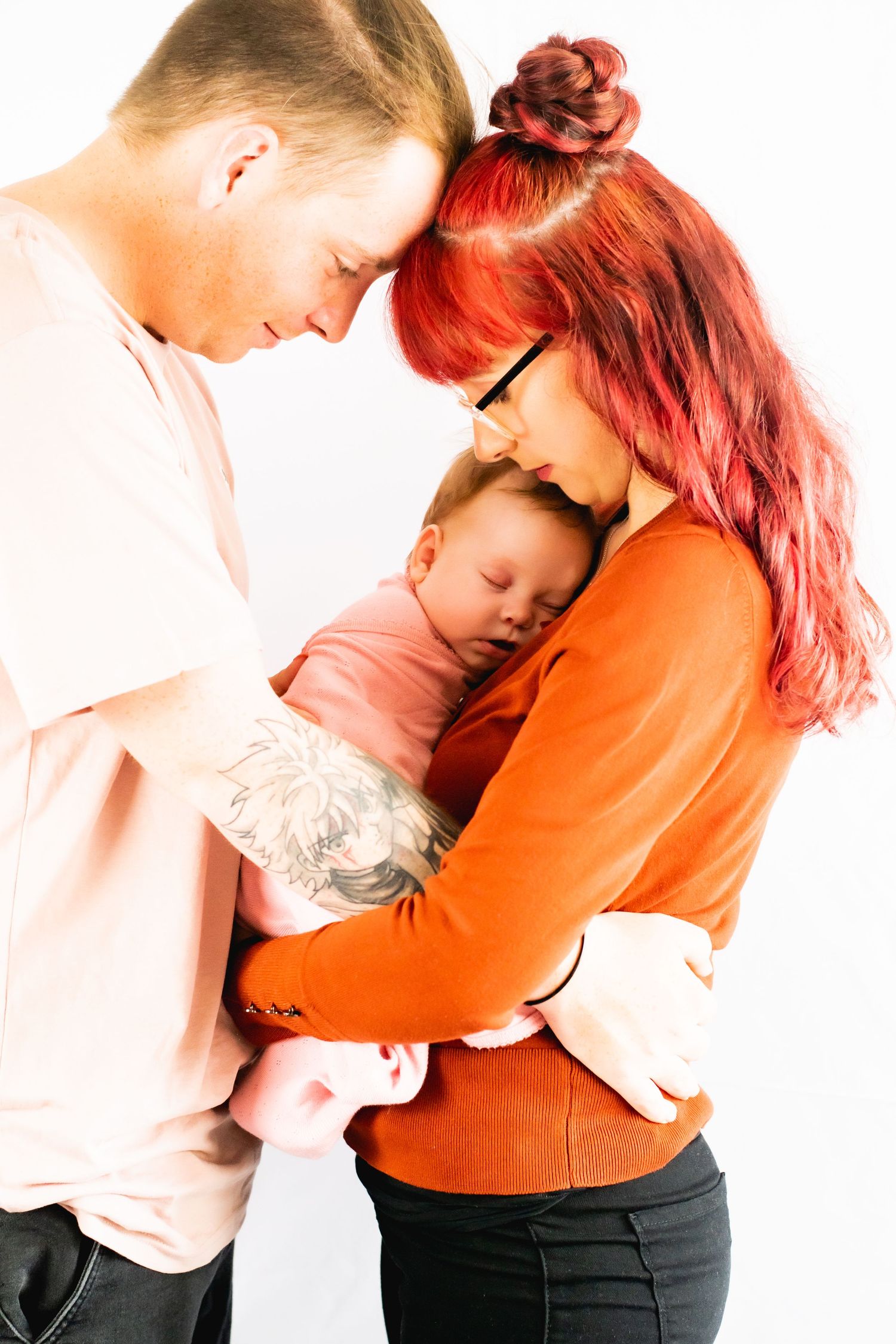A couple in contrasting shirts embrace while holding their sleeping baby.