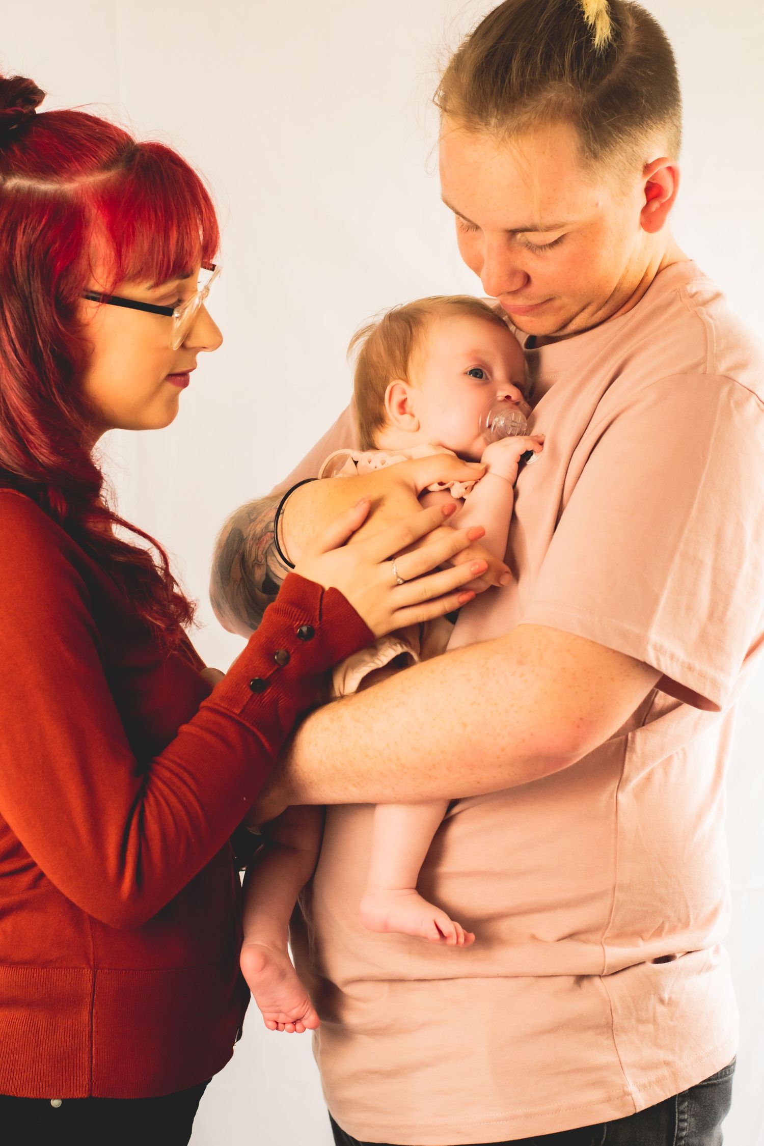 Parents in red and beige outfits holding their small infant during an intimate photo session.