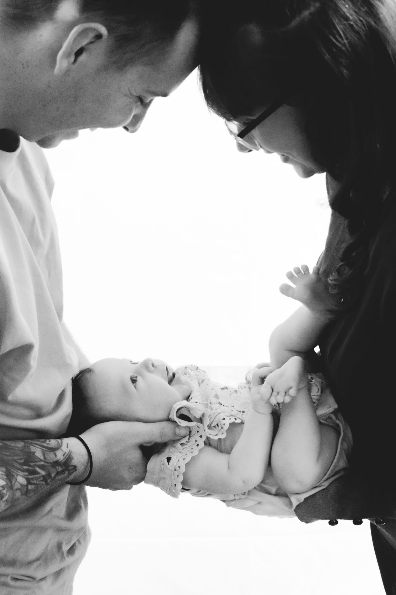 Black and white overhead shot of parents gazing down at their baby in lace clothing.