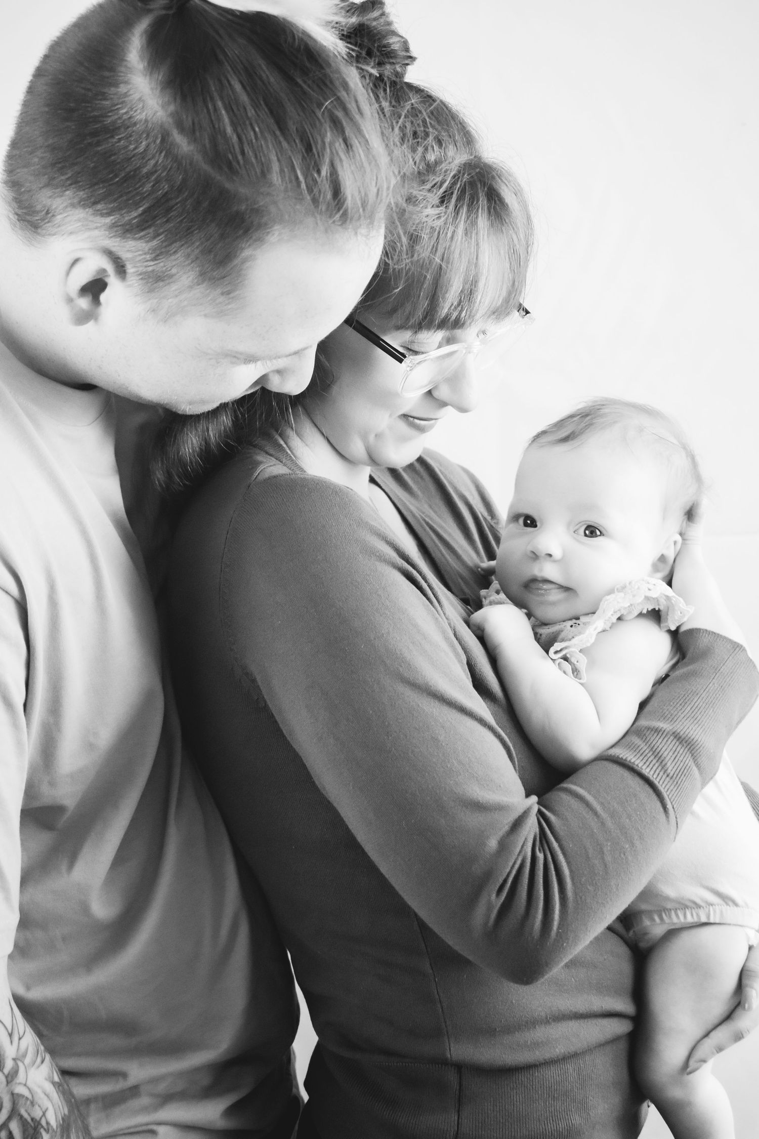 Black and white portrait of parents sharing tender moment with their infant.
