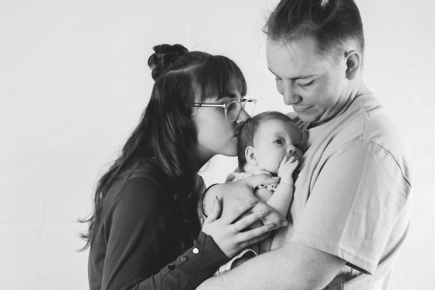 Black and white photo of a couple holding and admiring their baby together.