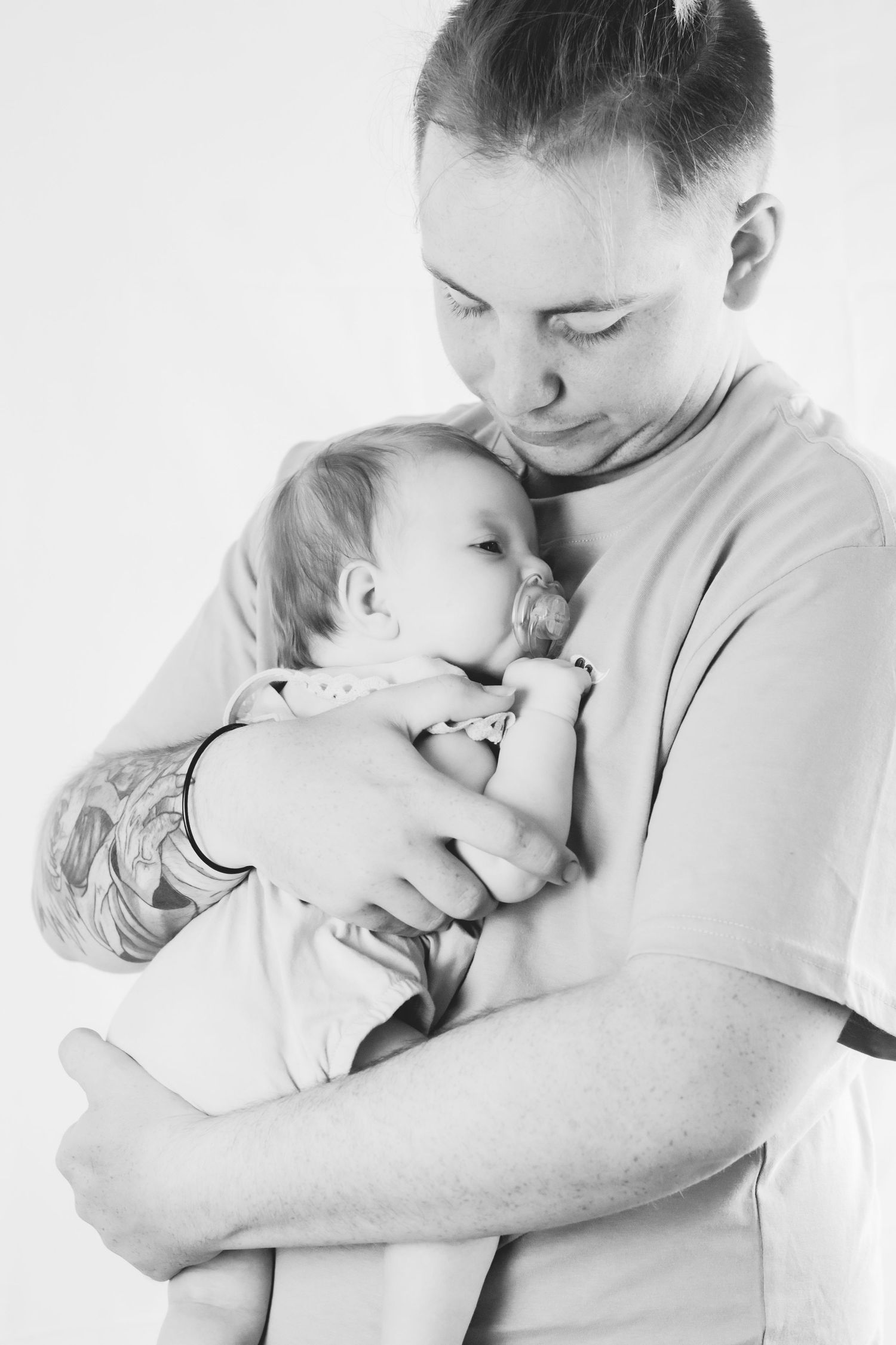 Black and white portrait of parent embracing sleeping baby against light background.