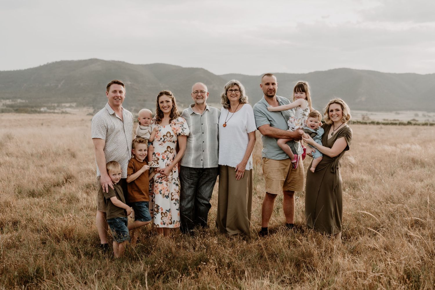 A multigenerational family poses together in a golden field with mountain views.