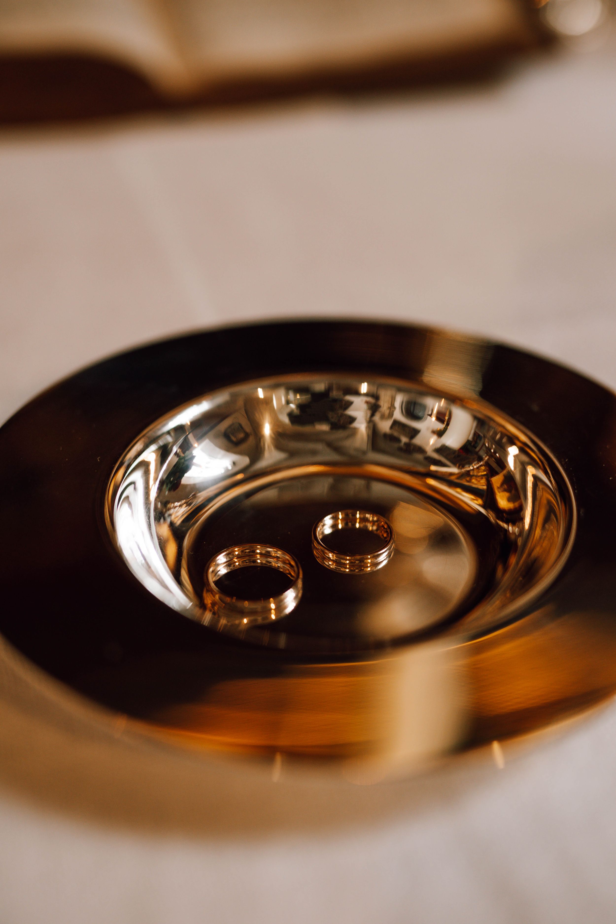 Two golden wedding rings reflect in a polished metal plate creating an artistic composition.