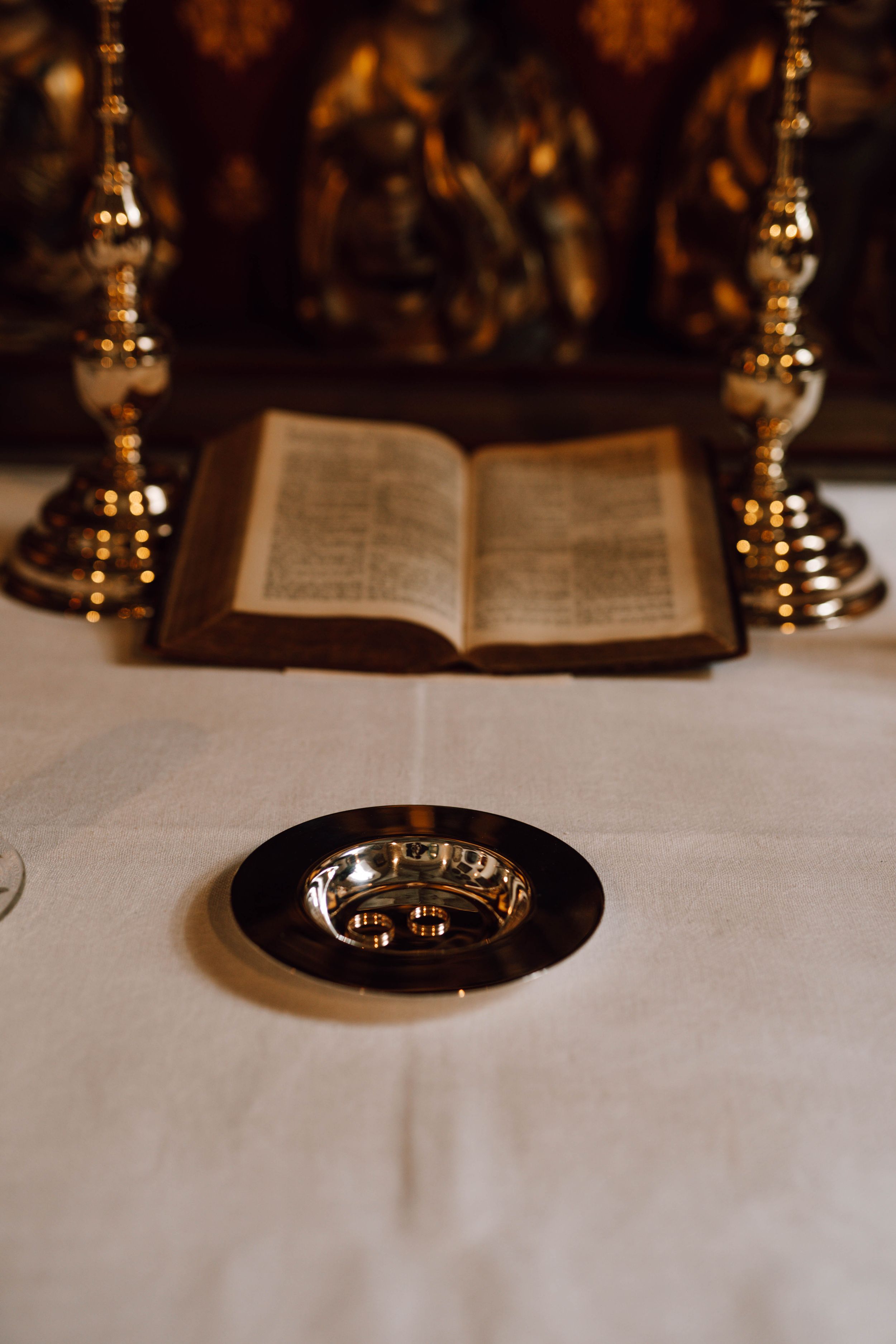 Vintage book between brass candlesticks with wedding rings on black plate.