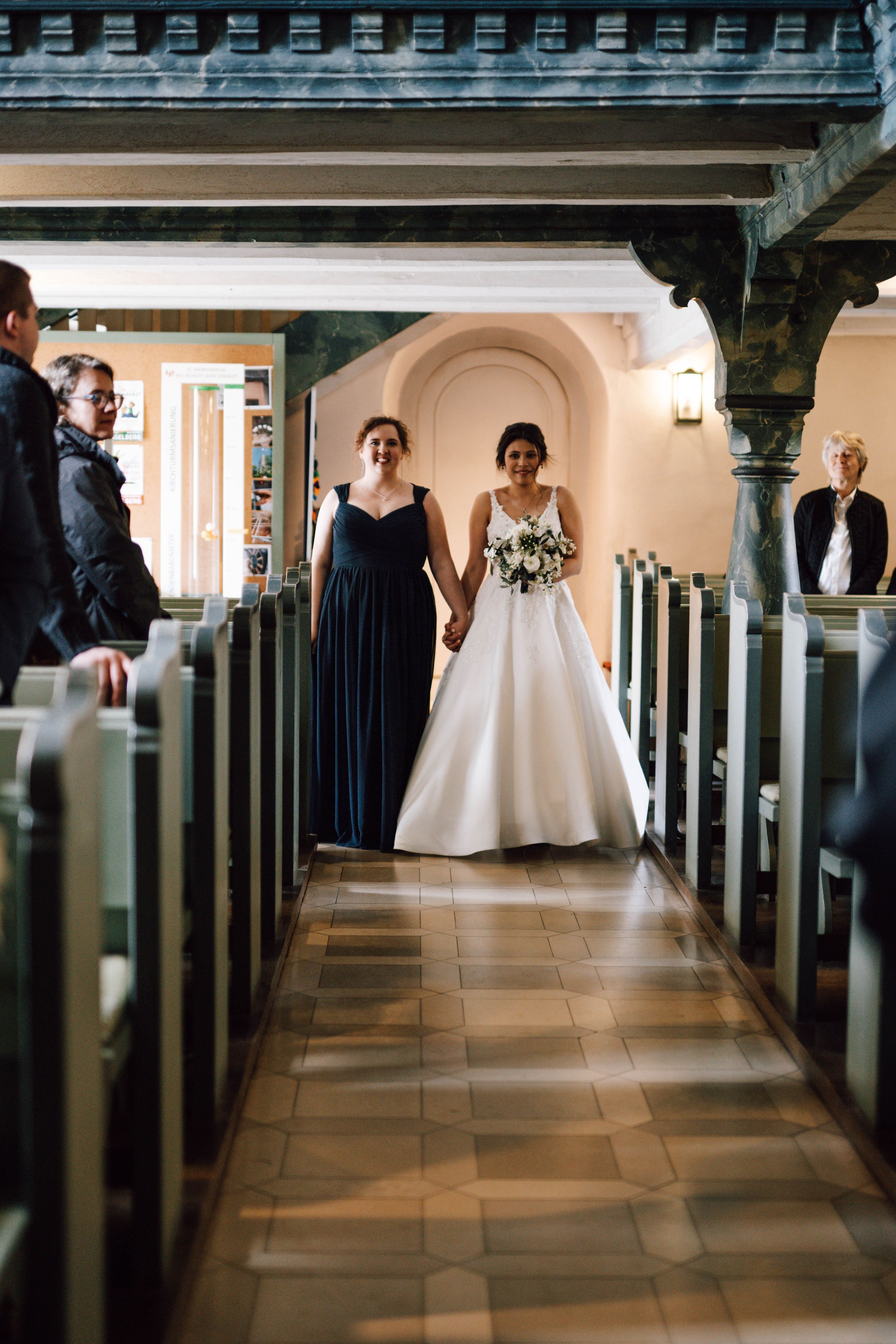 A wedding ceremony in a church aisle with traditional pews and arched architecture.