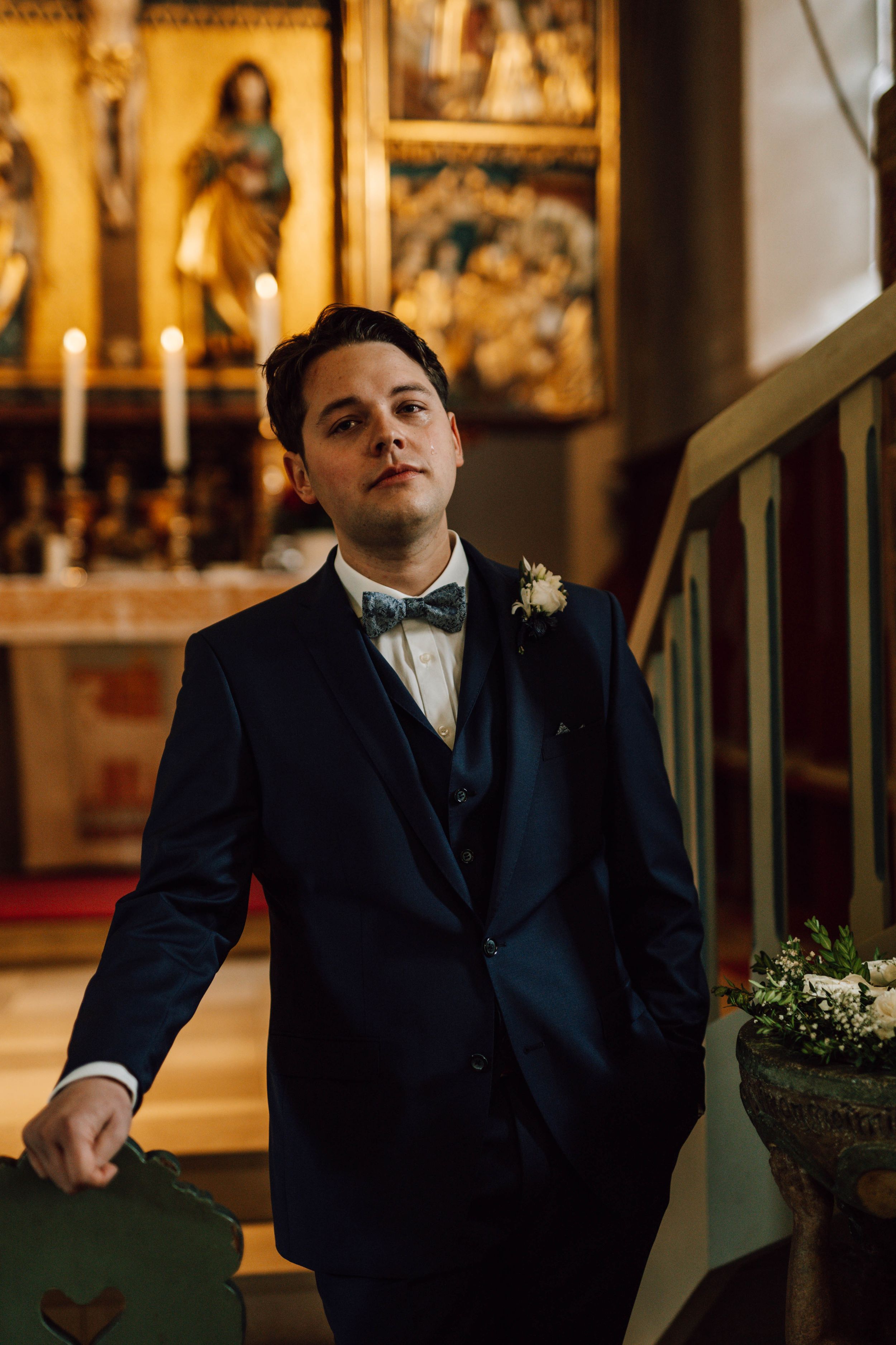 A formal wedding portrait in a church with ornate religious artwork in the background.