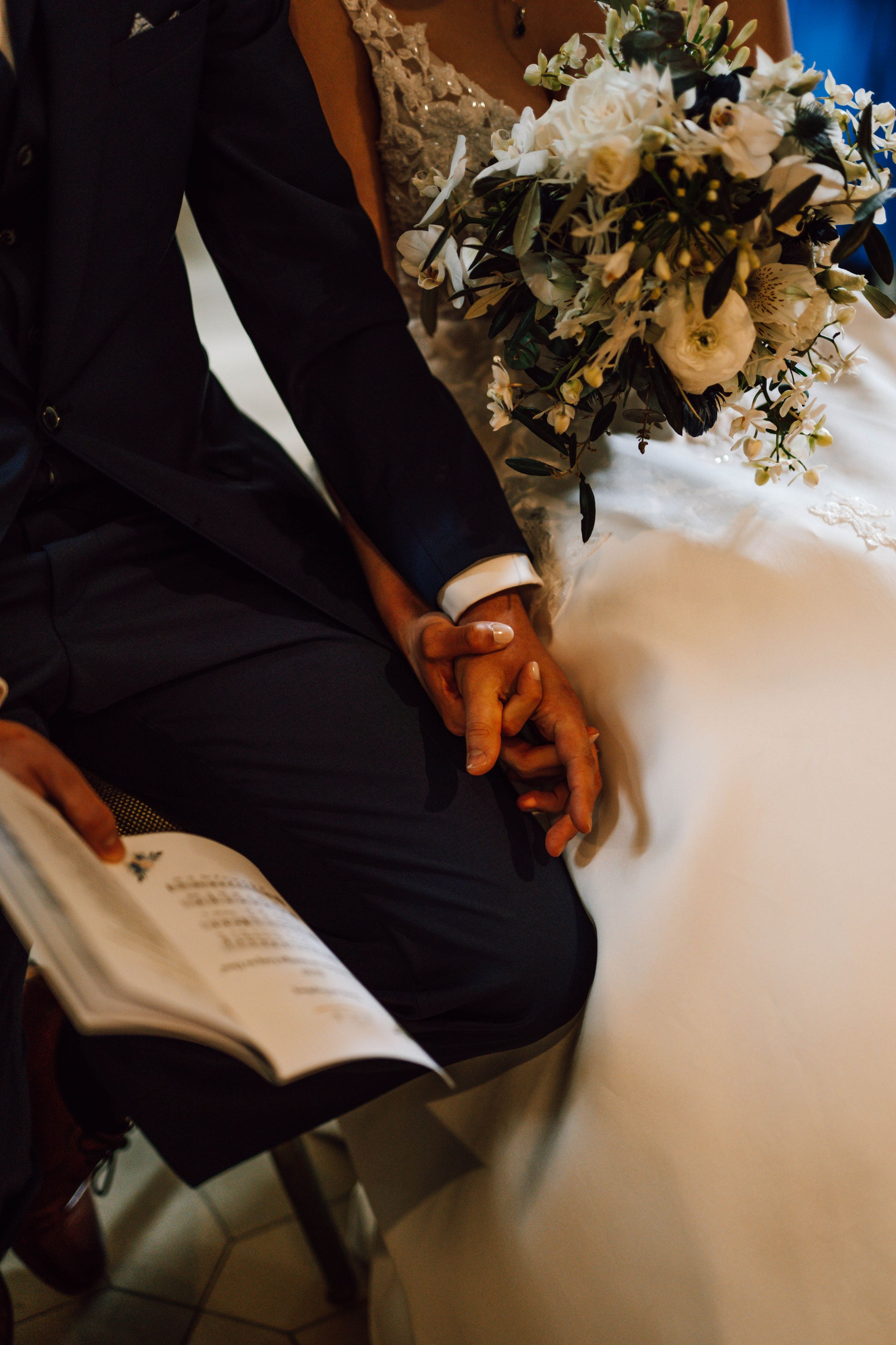Close-up of hands holding a wedding ceremony program with white floral bouquet.