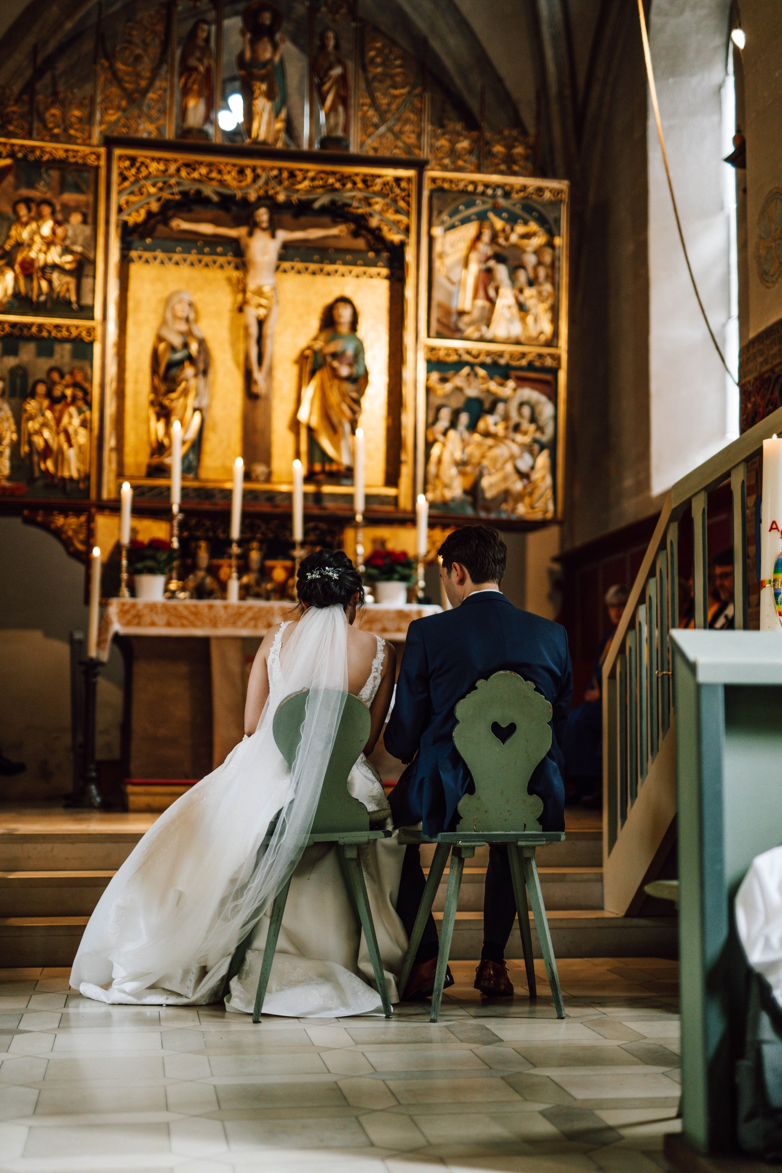 Newlyweds seated before an ornate golden altar in a historic church.