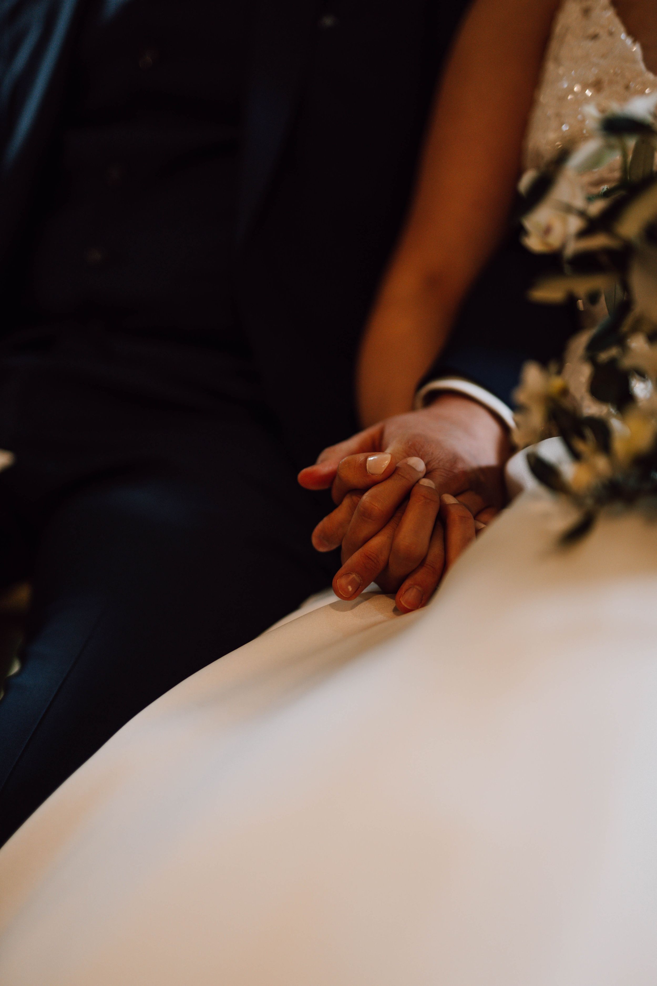 Close-up details of hands resting on a white wedding dress fabric.