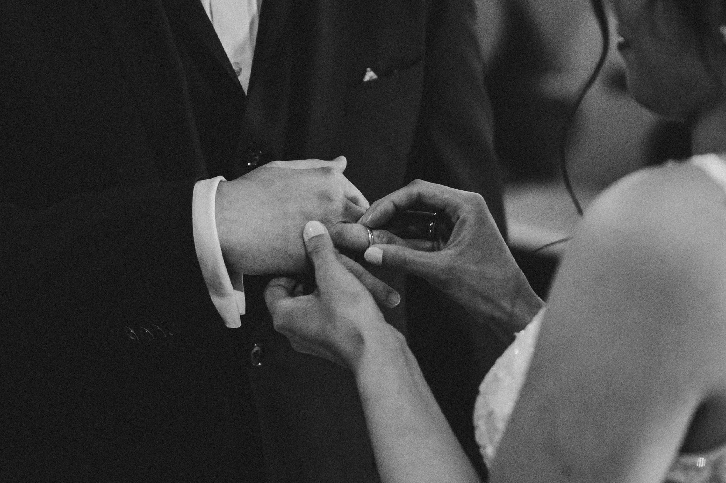 Black and white close-up of hands during a wedding ring exchange ceremony.