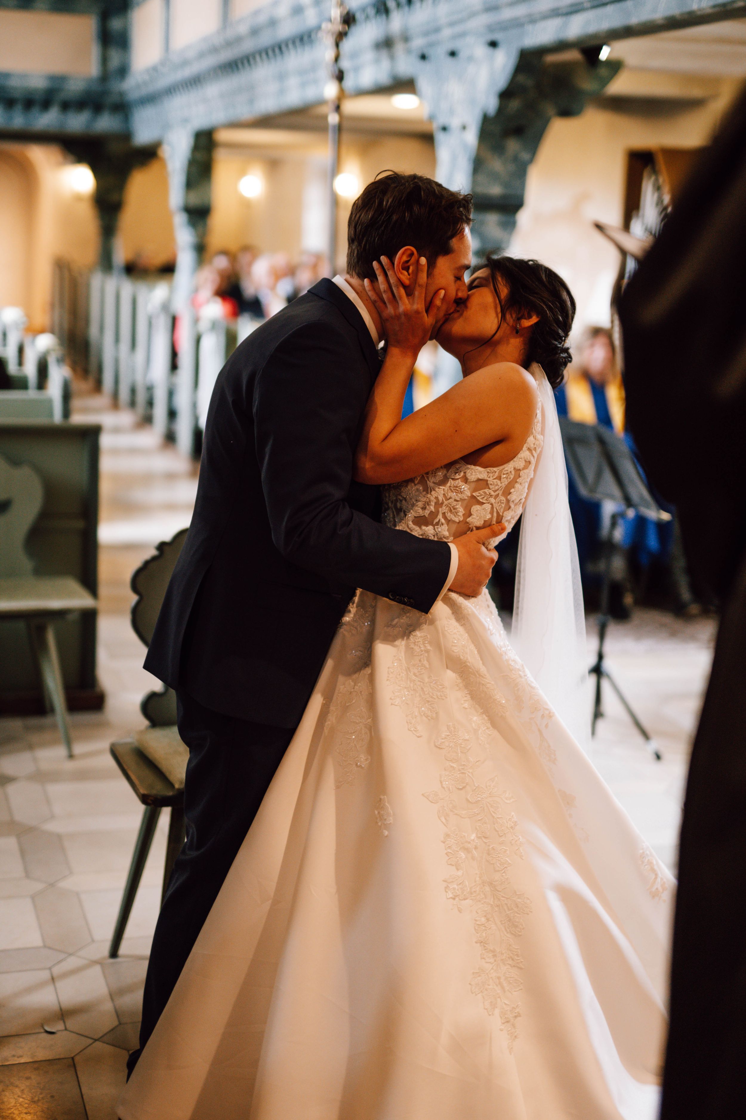 Romantic wedding kiss captured in a beautiful church setting with elegant architectural details.