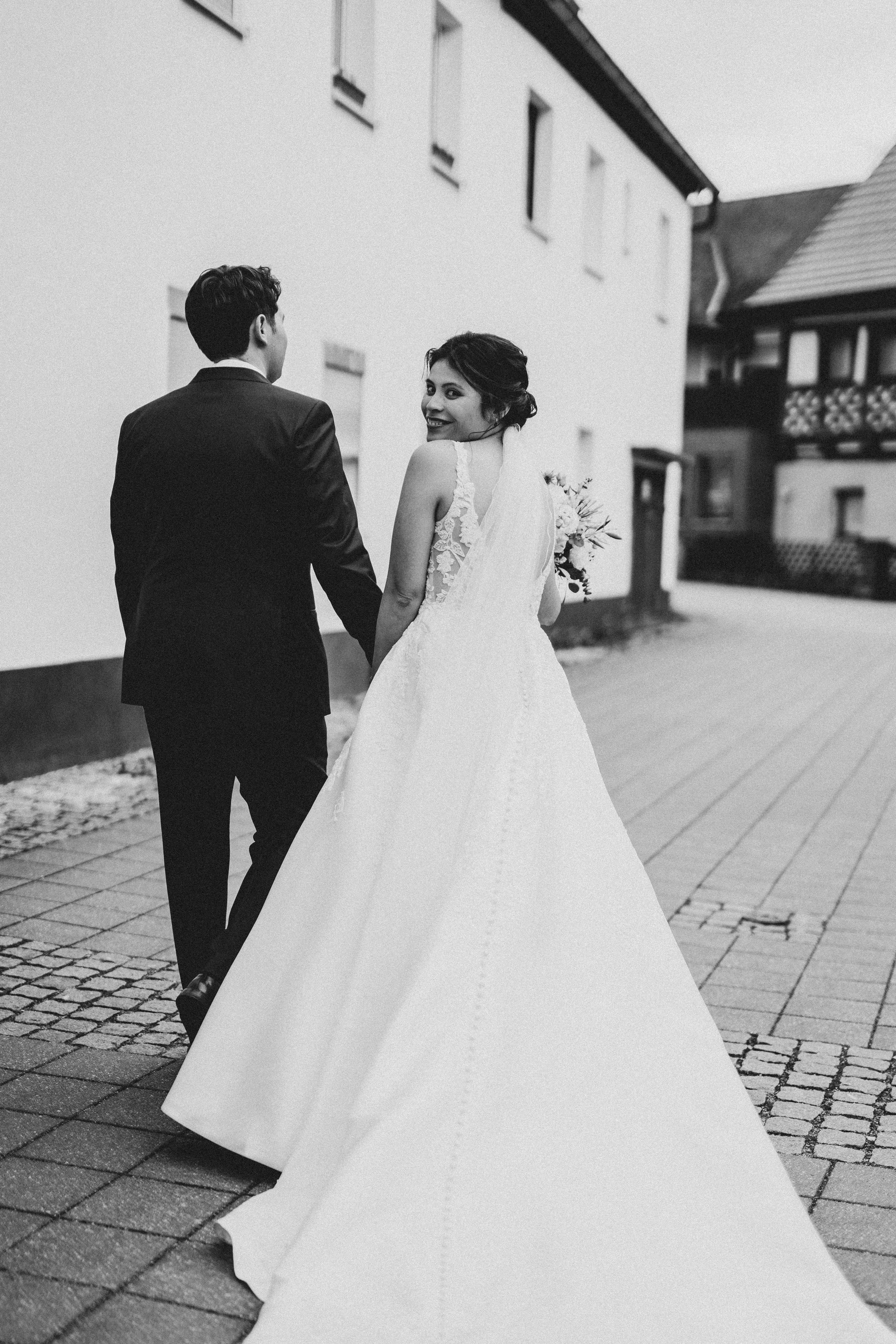 A wedding couple walks down a cobblestone street with the bride's white dress flowing behind them.