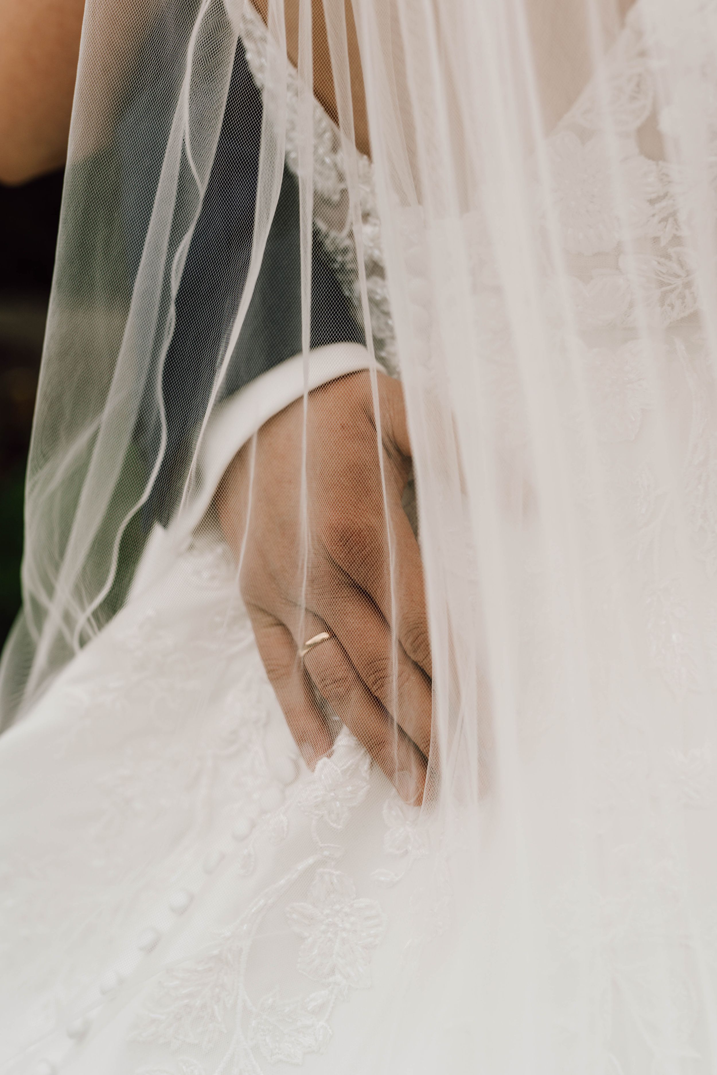 A delicate wedding veil drapes over a hand wearing a wedding ring.