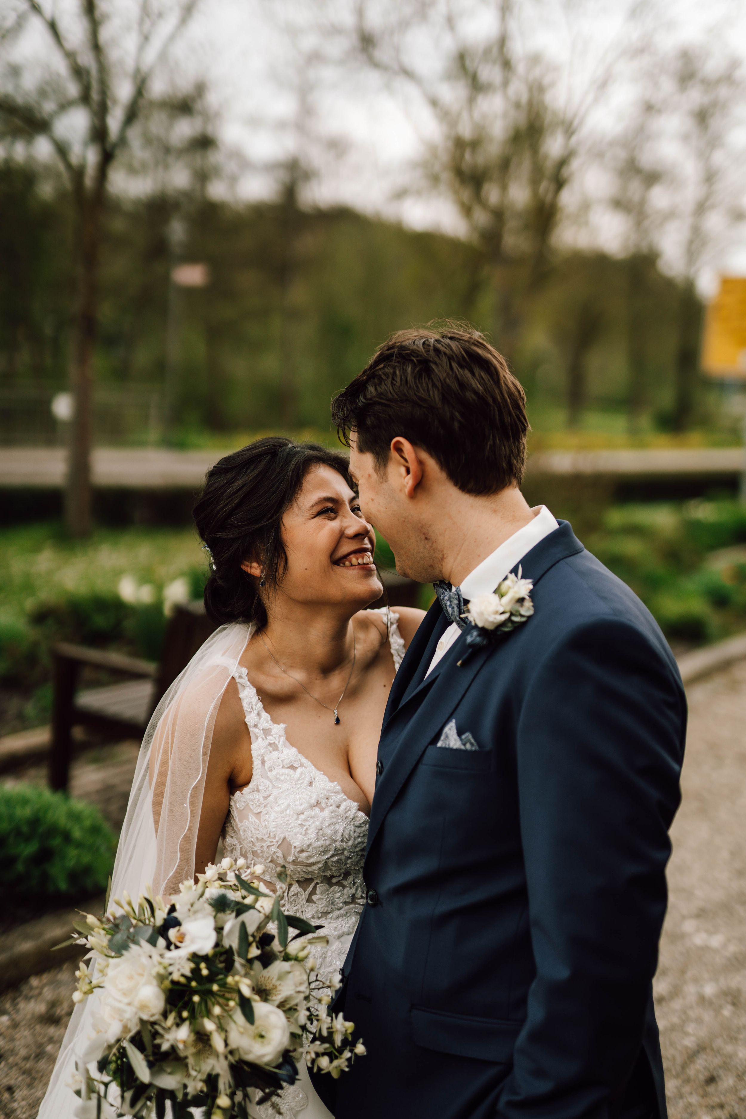 A joyful wedding couple shares an intimate moment in a garden setting with spring foliage.